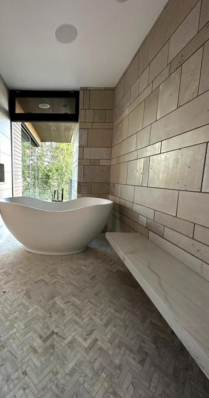 Long floating stone bench along a stone-look tile wall leading to a freestanding tub at the window
