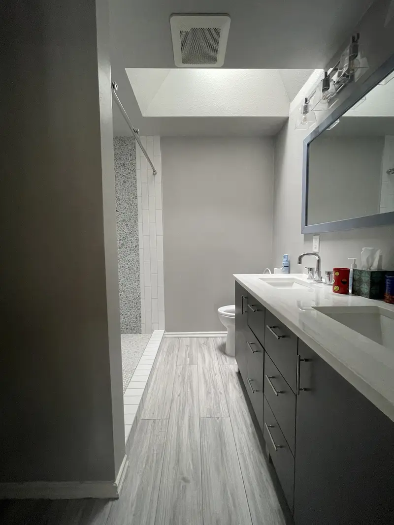 Long espresso double vanity with a white top facing a walk-in shower on gray plank tile