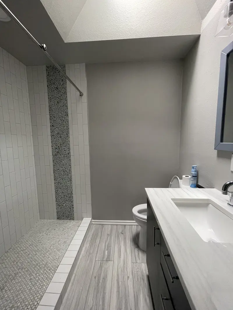 Walk-in shower with a gray mosaic stripe seen past the end of the white vanity top