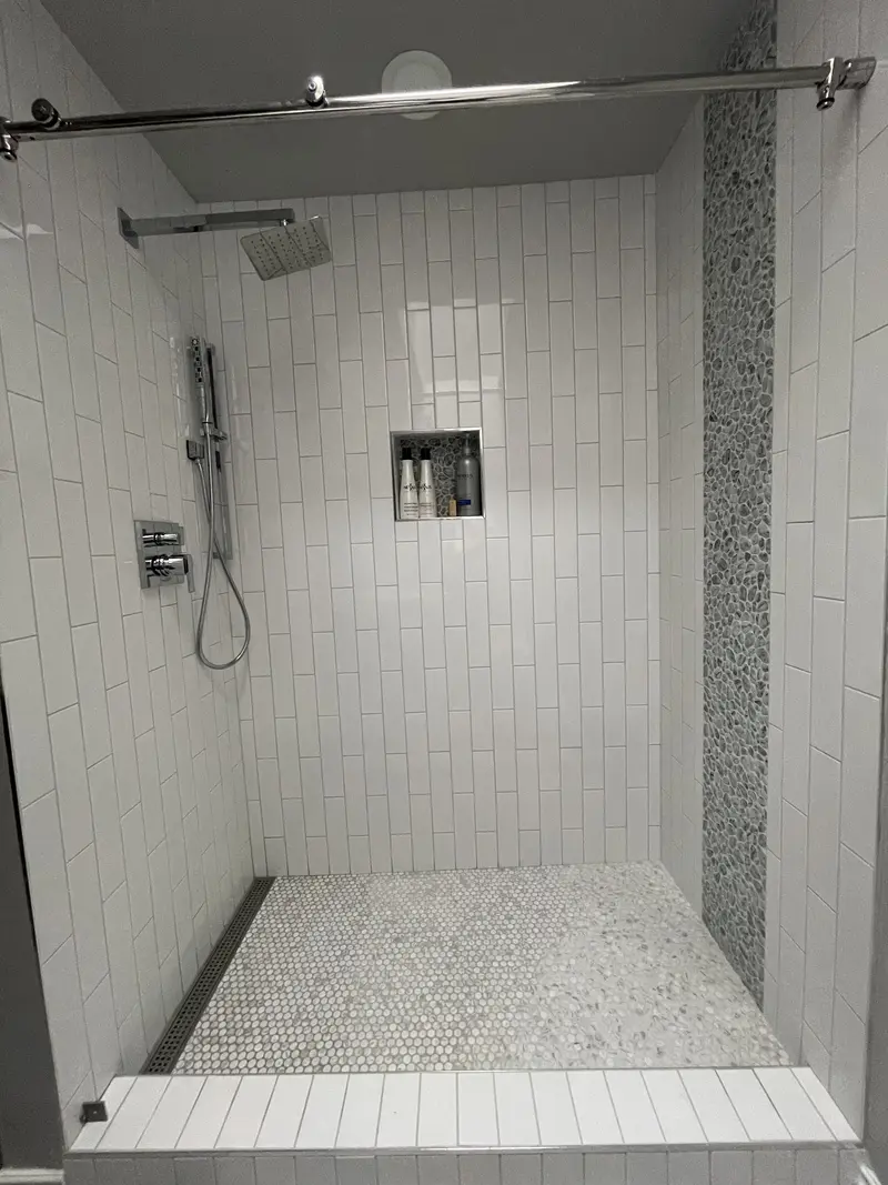 Shower niche between the rain head and handheld shower, with a glass panel hung from a ceiling rail