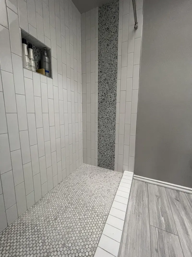 Penny tile shower floor with a white tile edge meeting the gray plank floor, and a niche above