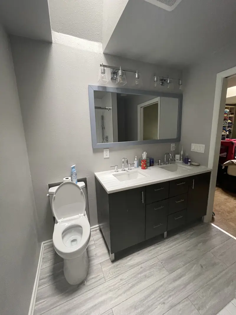 Toilet beside the espresso vanity on gray wood-look plank tile, with the wide mirror above