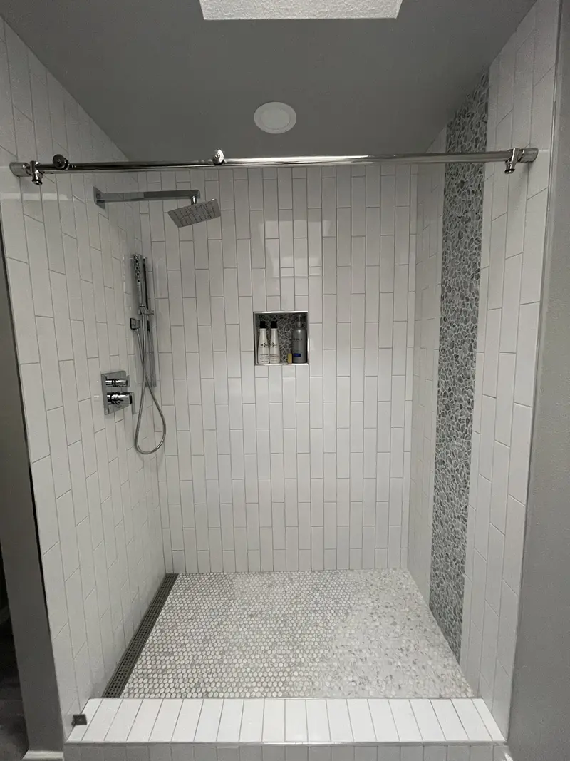 Walk-in shower with vertical white subway tile, a niche, rain head, handheld shower and penny tile floor
