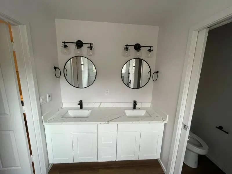 White shaker double vanity with two round black mirrors and a black light bar