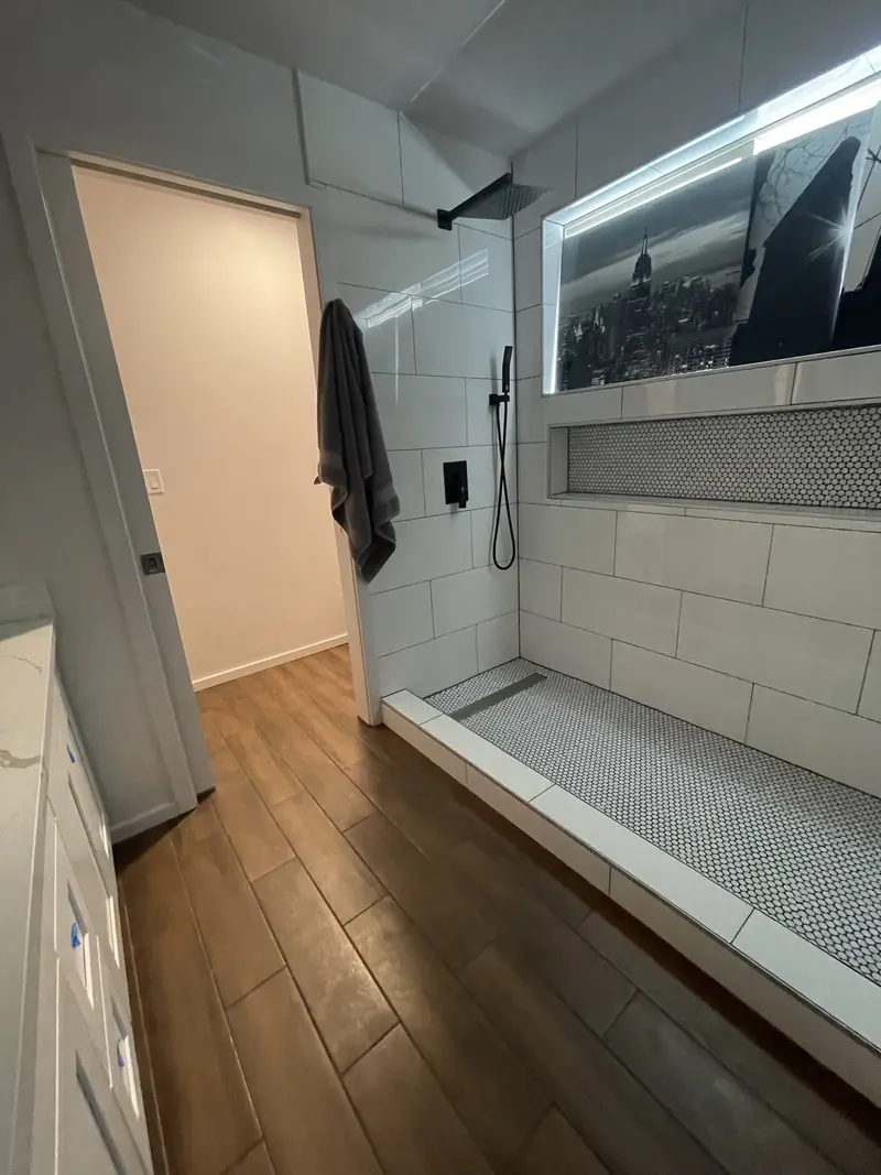 Long walk-in shower with a white penny tile floor next to a wood-look tile floor