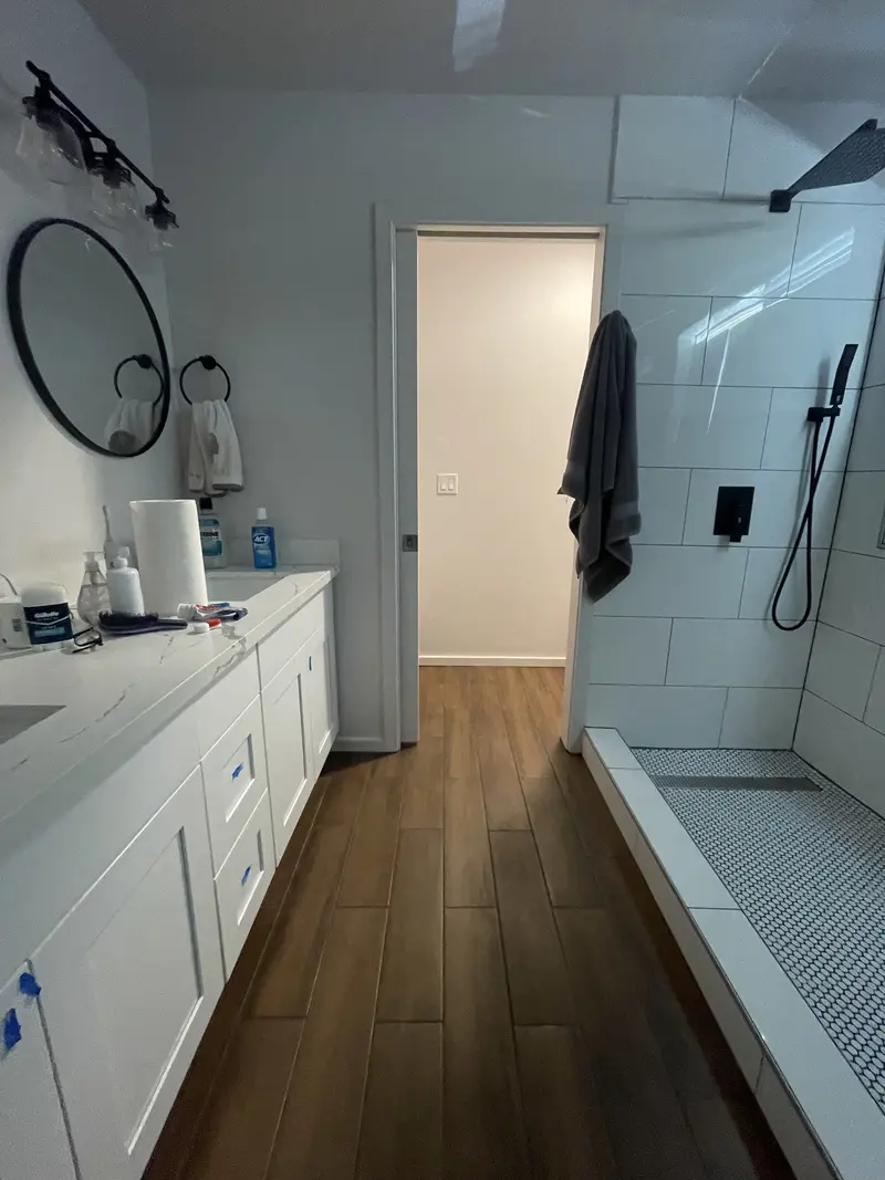 Master bathroom with a white double vanity on one side and a long walk-in shower on the other over a wood-look floor