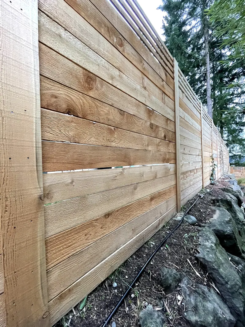 Close view down a horizontal cedar fence showing the board grain, posts and slatted top band above a rock wall