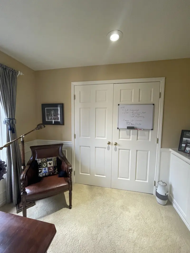 Office corner with white double doors, a leather chair and white wainscot panels