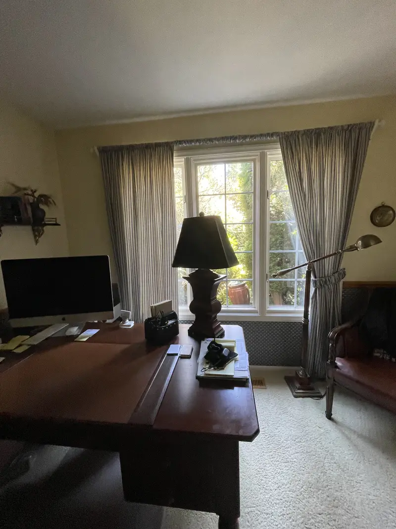 Office window wall with gray curtains and dark lattice panels on the lower wall behind the desk