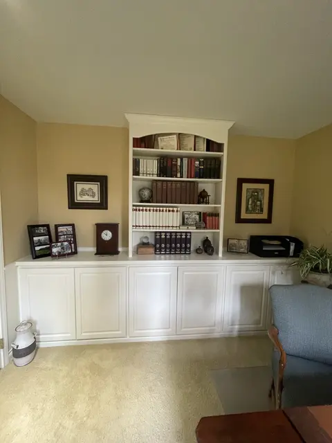 Home office with white base cabinets and a white arched bookcase filled with books, framed photos on the counter