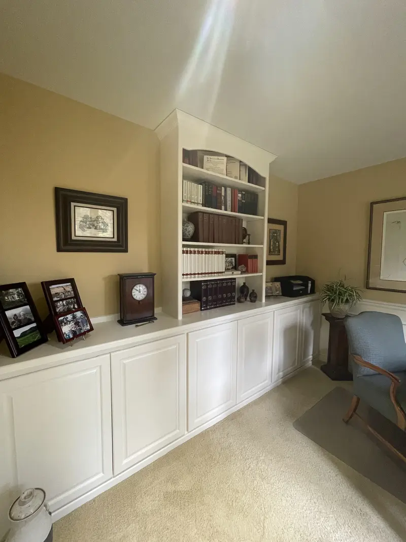 Angled view of the long run of white base cabinets and the white bookcase in the office