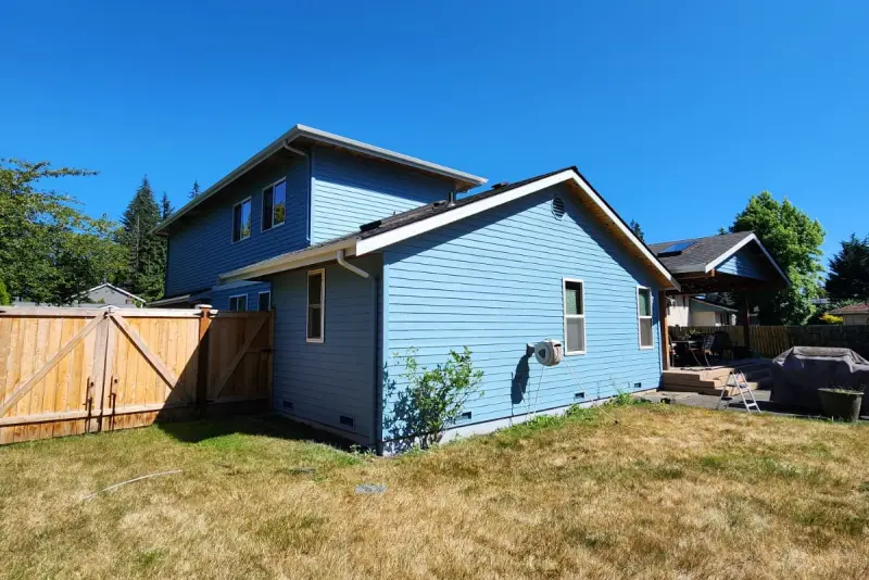 Back of a two story house in Marysville, WA with its lap siding repainted blue and white trim, seen across the lawn