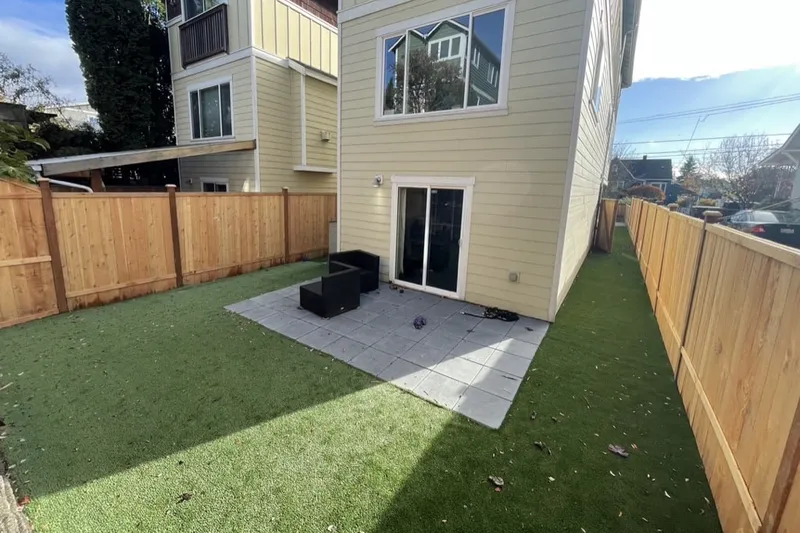 Square paver patio with outdoor seating beside the back door, set into artificial turf inside a new cedar fence in Seattle, WA