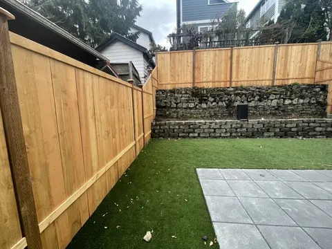 Corner of a square paver patio where it meets artificial turf along a cedar fence in Seattle, WA