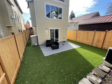 Paver patio with two outdoor chairs next to the back door, with turf and cedar fencing around it in Seattle, WA