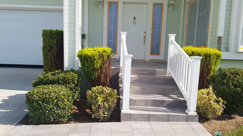 Front porch steps finished in large gray tiles between white railings, leading to the front door of a green house