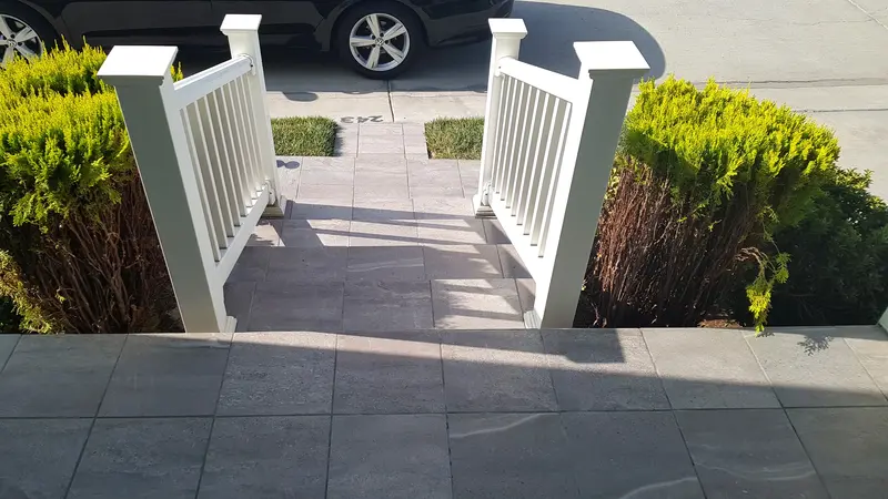 View from the tiled porch landing down the steps between white railings toward the street and a parked car