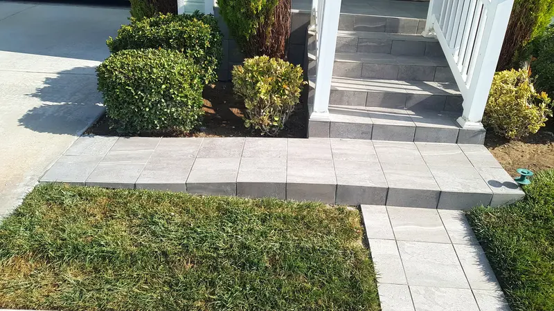 Light gray tile walkway running along a planting bed from the porch steps to the driveway, beside a lawn