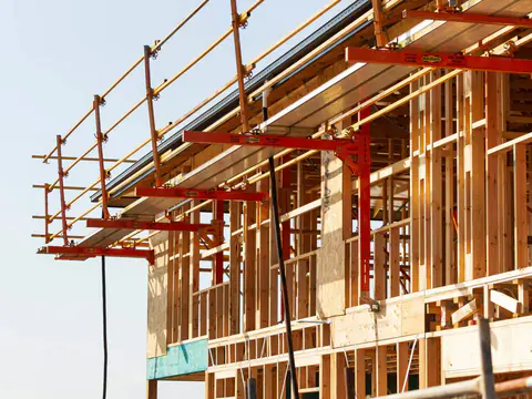 Timber framing of a building under construction, with steel scaffolding brackets along the upper floor