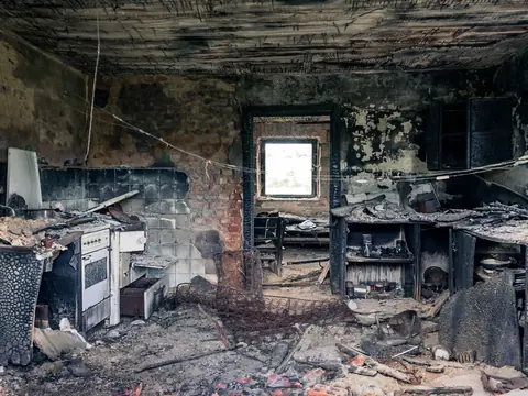 Kitchen interior charred by a house fire, with soot-blackened walls and ceiling