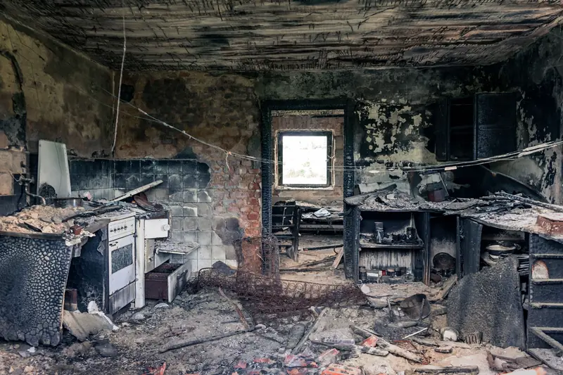Kitchen interior charred by a house fire, with soot-blackened walls and ceiling