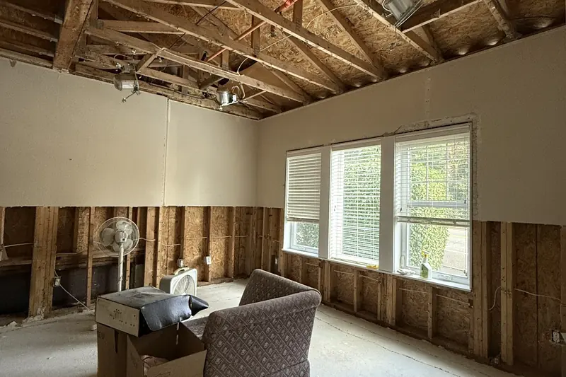 Living room with the ceiling drywall and lower walls removed after a water leak, under an insurance claim