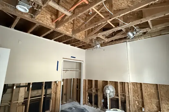 Room with the water-damaged ceiling drywall and lower walls removed after a leak, joists and studs exposed