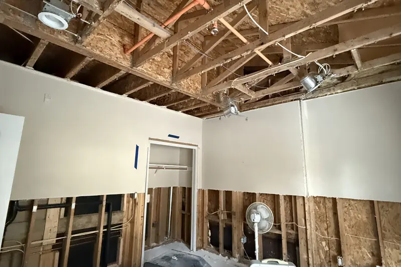 Room with the water-damaged ceiling drywall and lower walls removed after a leak, joists and studs exposed