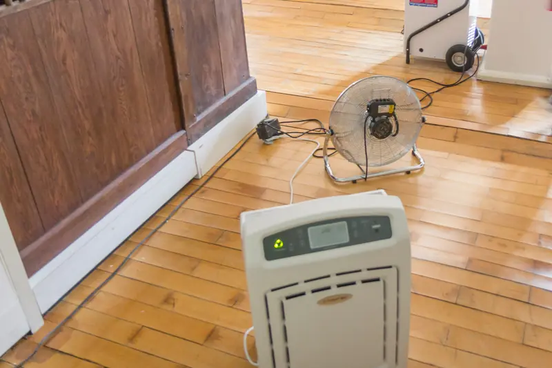 Dehumidifier and fan drying a wet hardwood floor