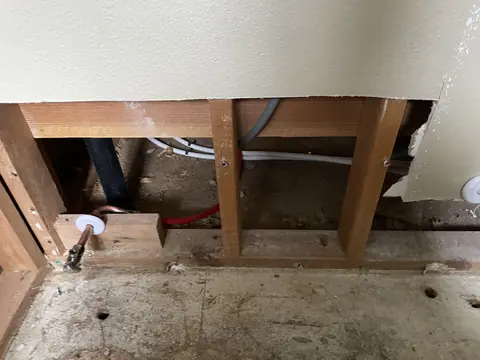 Drywall cut away above the floor after a water leak, exposing studs and subfloor