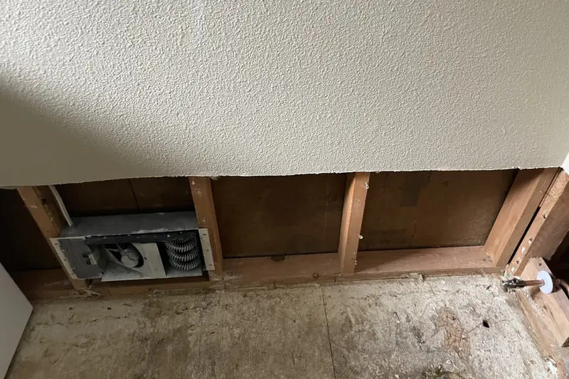 Drywall cut away above the floor after a water leak, exposing studs and subfloor