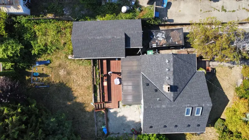 Drone view straight down on a house and a detached garage, both roofed in gray asphalt shingles, with two skylights and a chimney cap