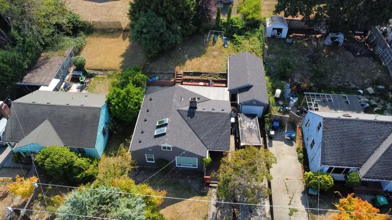 Higher drone view of the gray shingle roof among the neighboring houses and yards
