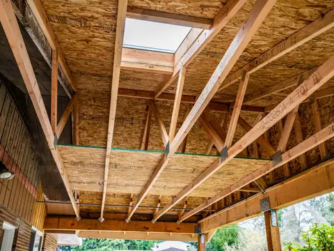 Underside of a new carport roof showing wood trusses, sheathing and a skylight in Auburn, WA