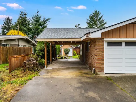 Driveway view of a carport under a gray shingle roof beside a brick garage in Auburn, WA