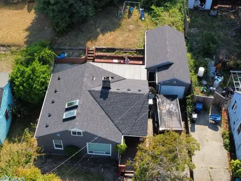 Overhead drone view of a repaired dark shingle roof with two skylights and a chimney in Seattle, WA