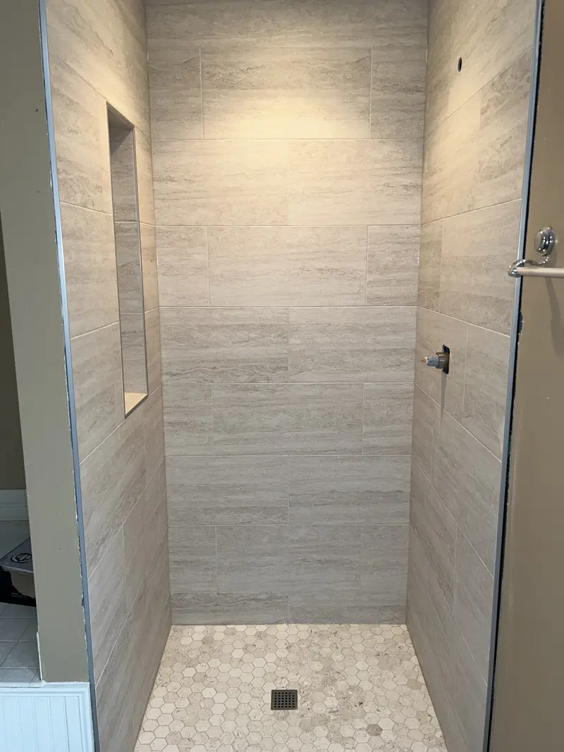 Shower walls tiled in light gray plank tile with a recessed niche on the side wall