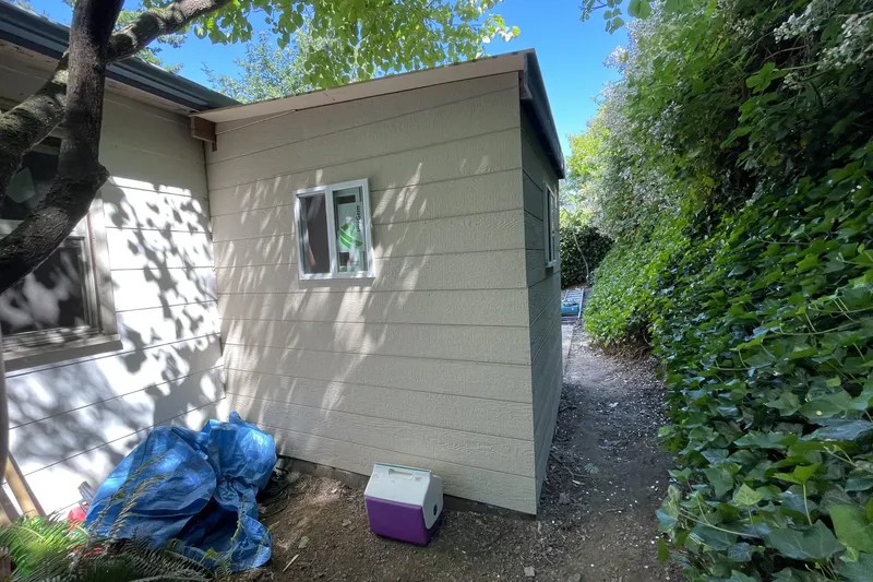 Tan lap siding and a small white window on a new shed built beside a house in Seattle, WA