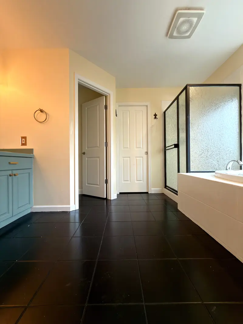 Master bathroom before the remodel with a dark tile floor, a blue-green vanity and a framed shower with textured glass