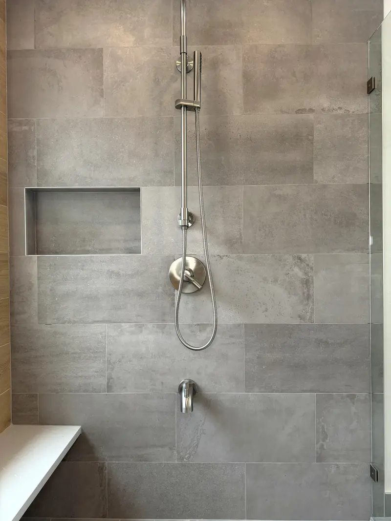 Walk-in shower in large gray tile with a long recessed niche, a handheld spray on a slide bar and a bench