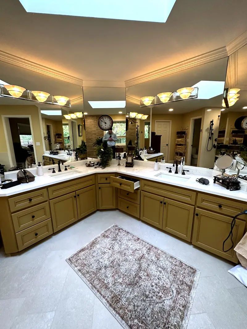 Long L-shaped double vanity with white tops and two sinks under mirrors and a skylight