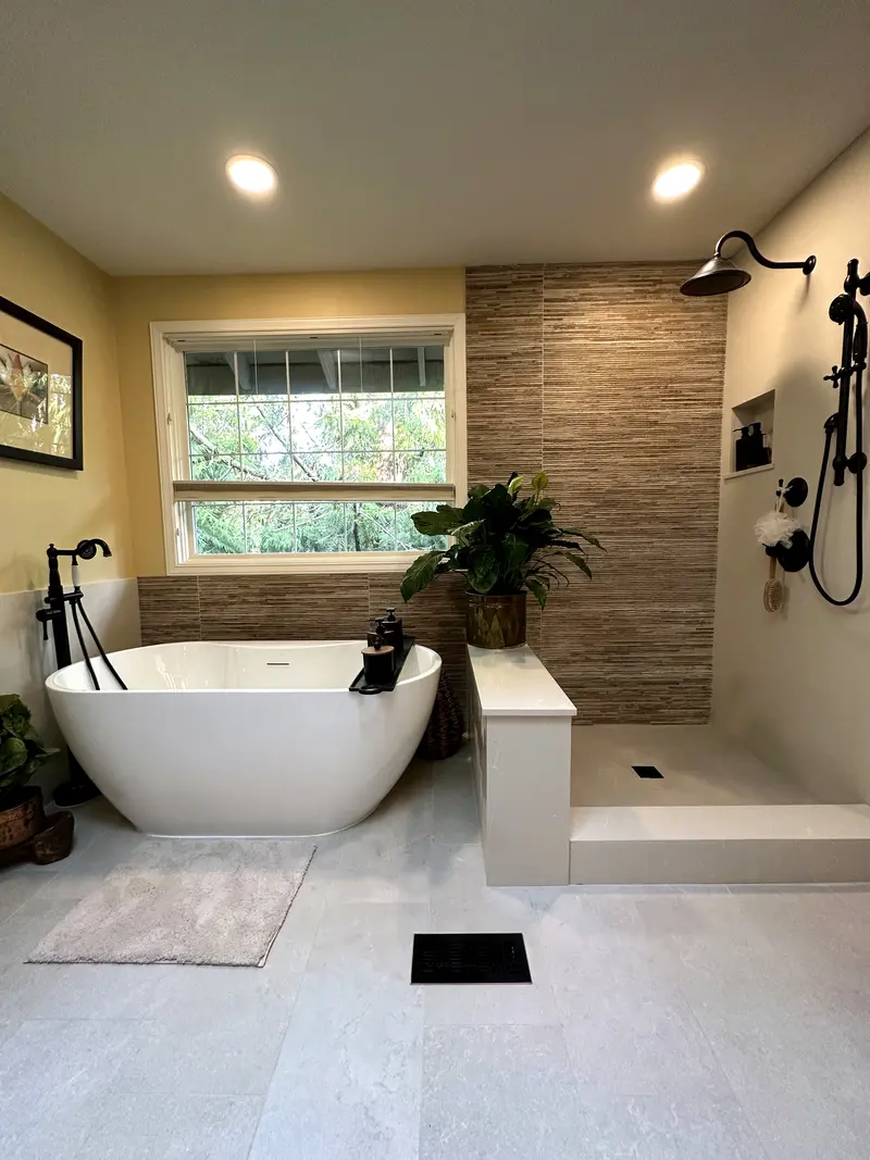 White freestanding tub with a dark floor-mounted filler beside a walk-in shower with a stacked stone accent wall