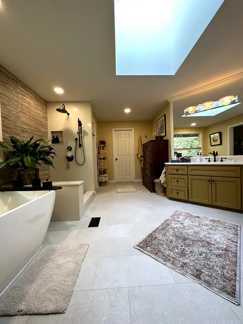 Wide view of the master bathroom under a skylight, from the tub and shower across a light gray tile floor to the vanity