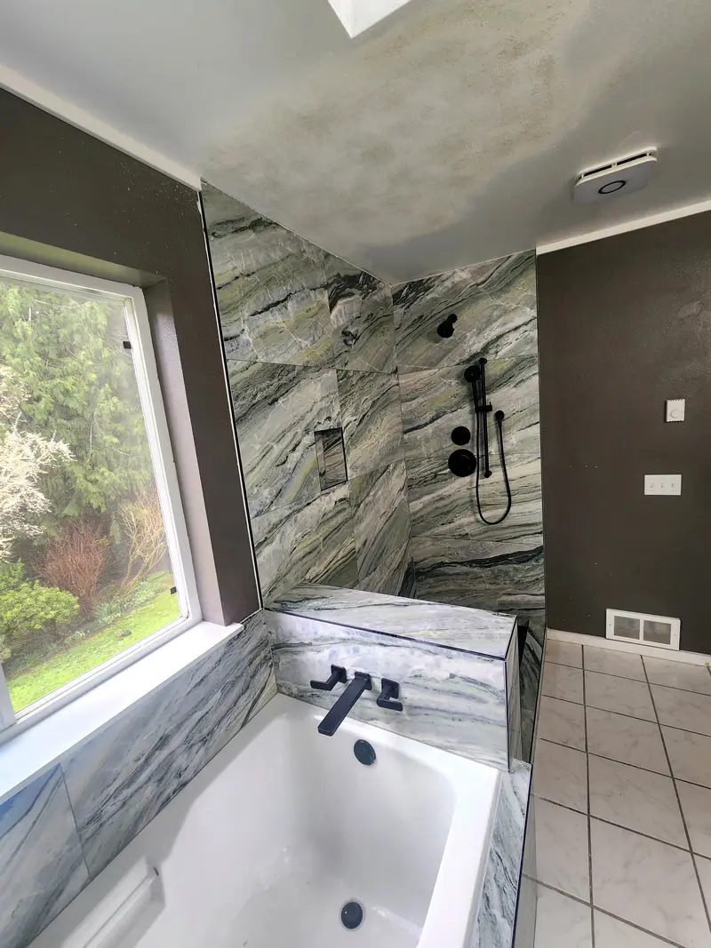 Drop-in tub under a window with a veined stone-look surround and a matte black wall-mounted filler
