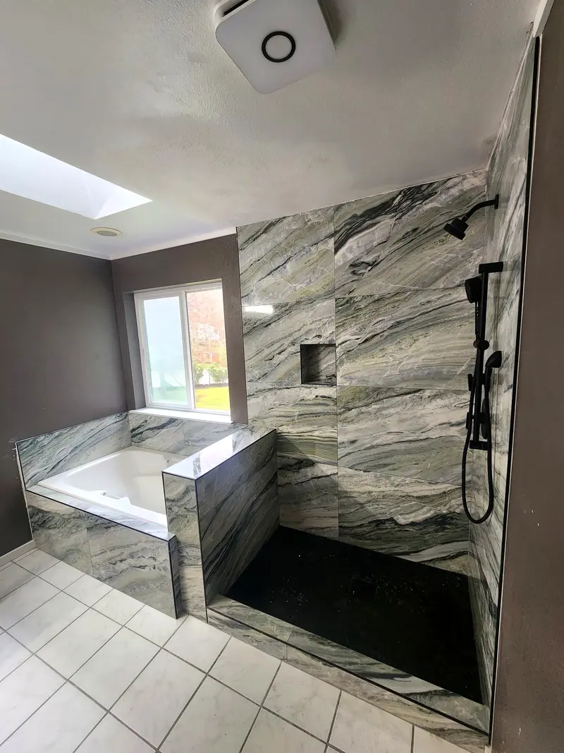 Master bathroom with a walk-in shower and tub surround in gray veined stone-look tile under a skylight