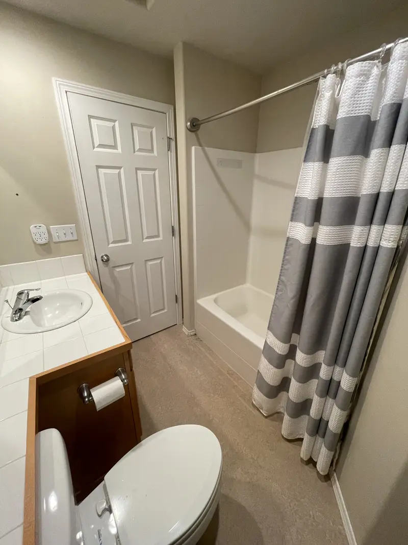 Old tub and shower with a striped curtain beside the bathroom door and the end of the vanity