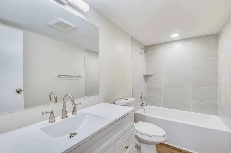 Hall bathroom with a white vanity, wide mirror and a tiled tub surround