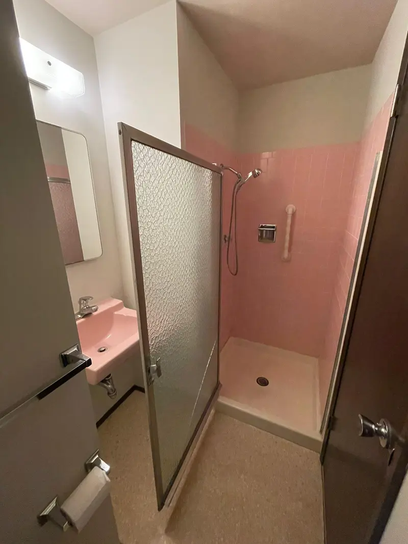 Original bathroom with a pink tiled shower and framed glass door