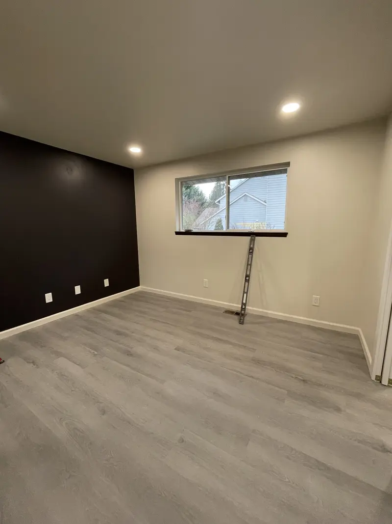 Bedroom with a black accent wall, gray plank floor and recessed lights