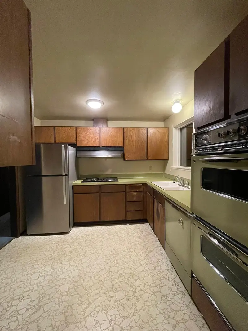 Original kitchen with dark wood cabinets, wall ovens and a speckled floor